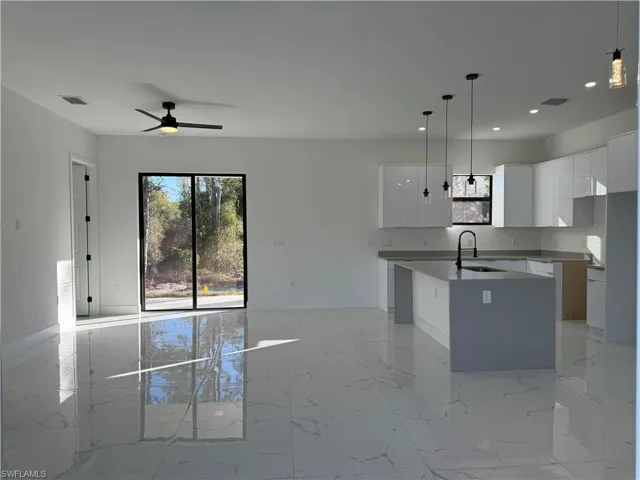 Kitchen with white cabinetry, sink, pendant lighting, and a center island with sink