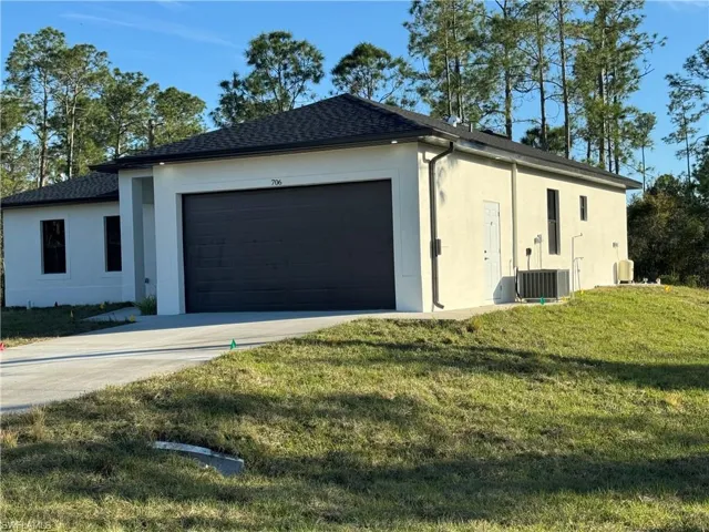 View of side of property with a garage, a lawn, and central air condition unit