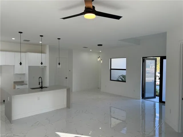 Kitchen featuring sink, decorative light fixtures, an island with sink, and white cabinets