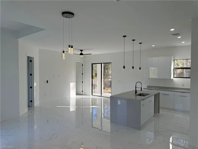 Kitchen with white cabinetry, sink, a center island with sink, and pendant lighting
