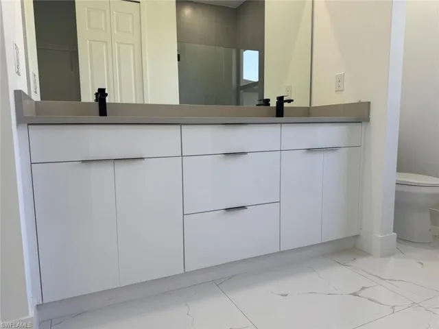 Bathroom featuring double vanity, toilet, and marble finish floor