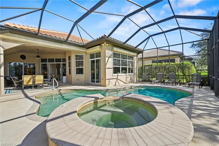 View of pool featuring a sunroom, a patio area, a pool with connected hot tub, glass enclosure, and outdoor dining area