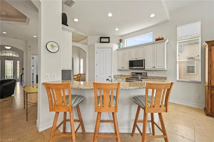 Kitchen with a kitchen bar, light stone counters, stainless steel appliances, plenty of natural light, and recessed lighting