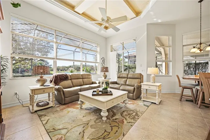 Living room featuring coffered ceiling, beamed ceiling, ceiling fan, light tile patterned floors, and a chandelier