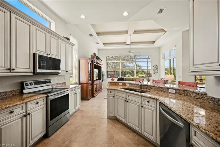 Kitchen featuring stainless steel appliances, coffered ceiling, healthy amount of natural light, light stone countertops, and beam ceiling