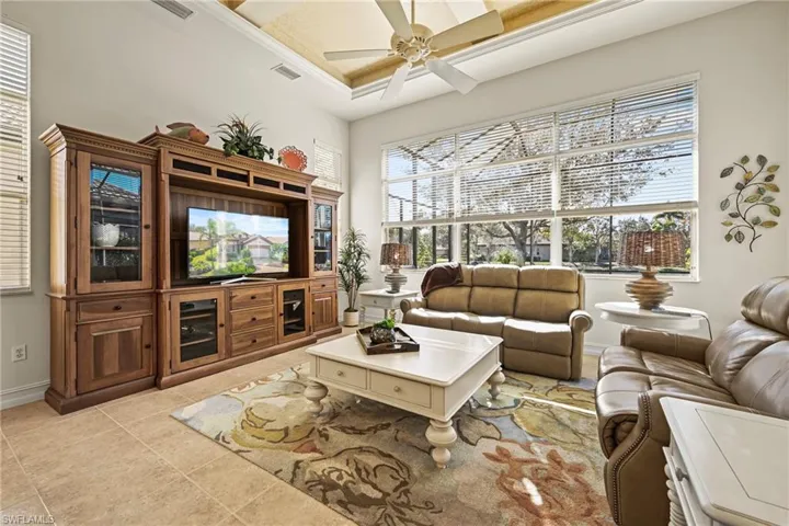 Living room with a ceiling fan, healthy amount of natural light, light tile patterned flooring, a raised ceiling, and a high ceiling