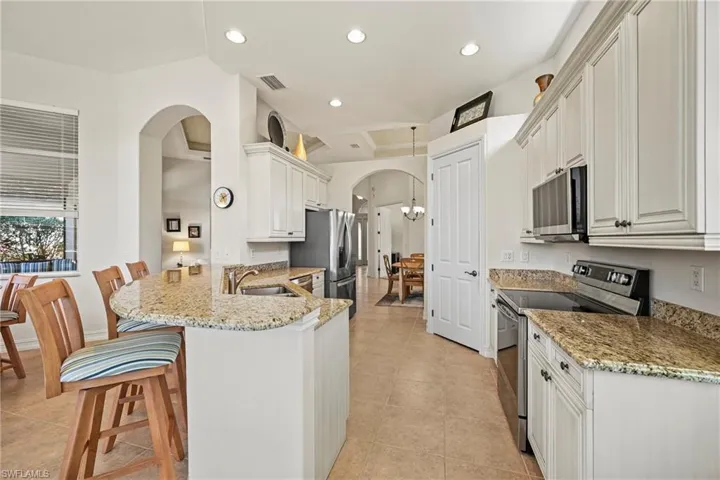 Kitchen with stainless steel appliances, arched walkways, a peninsula, light stone counters, and a breakfast bar area