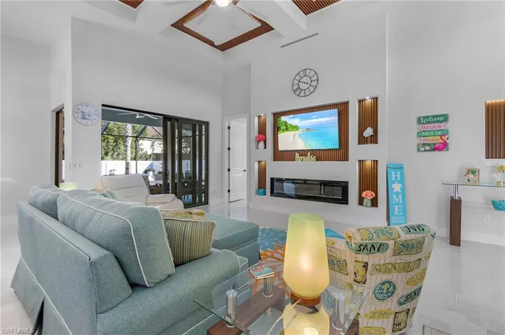 Living room featuring coffered ceiling, a glass covered fireplace, ceiling fan, beamed ceiling, and a high ceiling