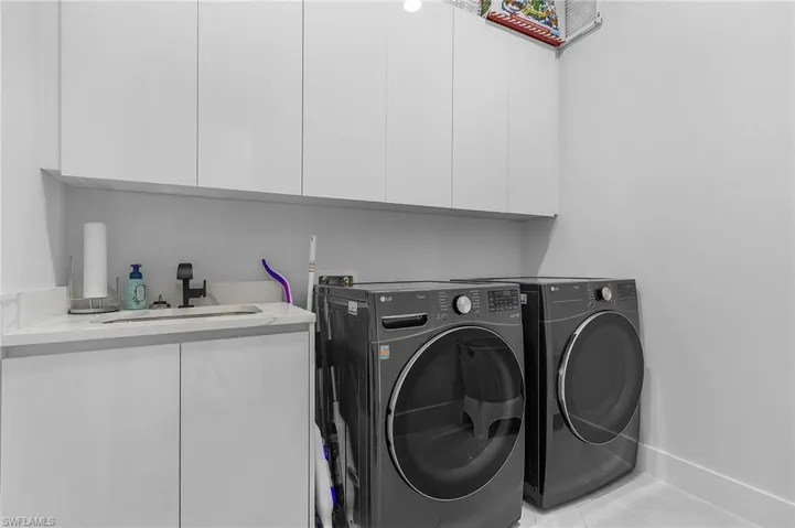 Washroom with light tile patterned floors, cabinet space, a sink, independent washer and dryer, and baseboards