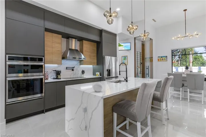 Kitchen with appliances with stainless steel finishes, a chandelier, wall chimney exhaust hood, and modern cabinets