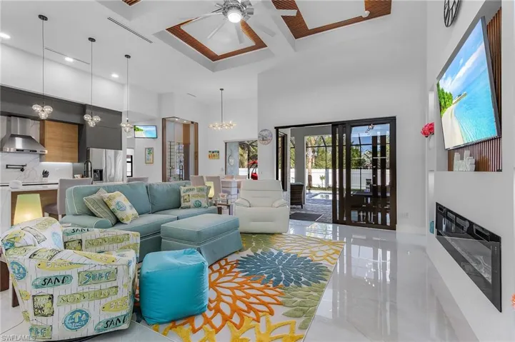 Living area featuring beam ceiling, a fireplace, a towering ceiling, coffered ceiling, and ceiling fan with notable chandelier