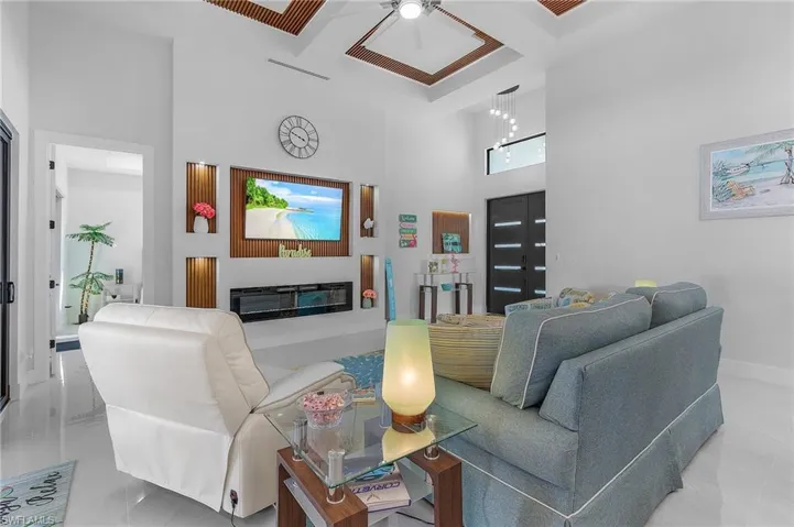 Living room with a high ceiling, coffered ceiling, baseboards, beamed ceiling, and a glass covered fireplace