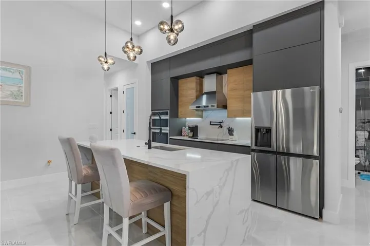 Kitchen with stainless steel appliances, decorative backsplash, a sink, modern cabinets, and wall chimney exhaust hood