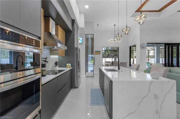 Kitchen with stainless steel appliances, a sink, wall chimney range hood, modern cabinets, and an inviting chandelier