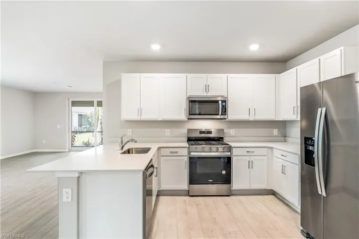 Kitchen with stainless steel appliances, a peninsula, light wood finished floors, white cabinetry, and recessed lighting