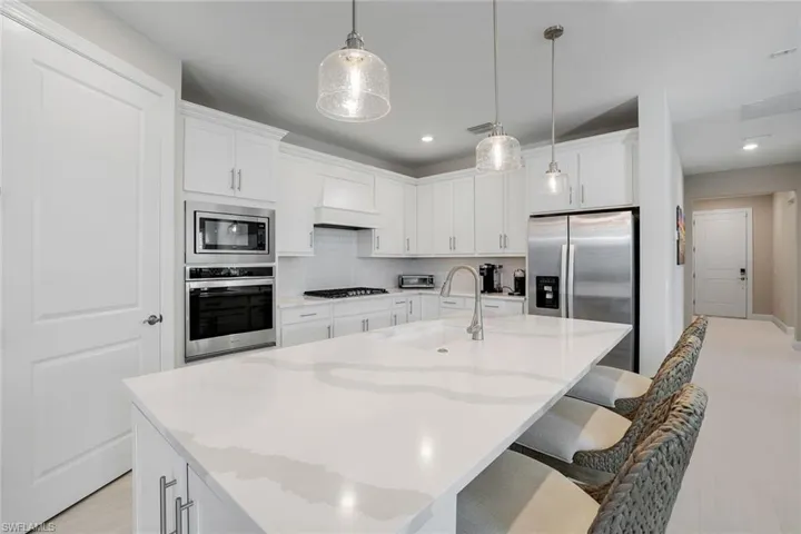 Kitchen featuring white cabinetry, stainless steel appliances, a kitchen breakfast bar, a kitchen island with sink, and backsplash