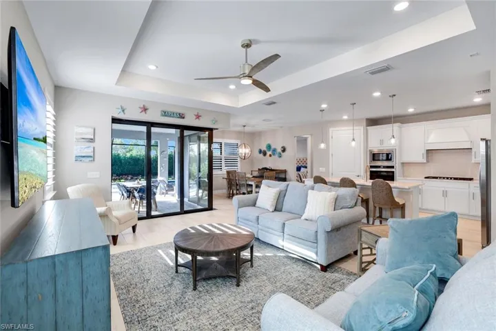 Living room with ceiling fan, light color tile floors, recessed lighting, and a tray ceiling