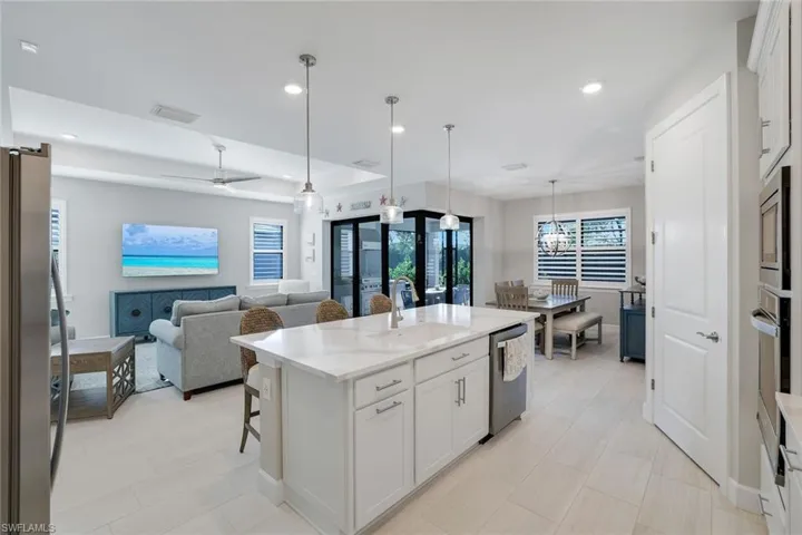 Kitchen with a breakfast bar, white cabinetry, light stone counters, stainless steel appliances, and a center island with sink
