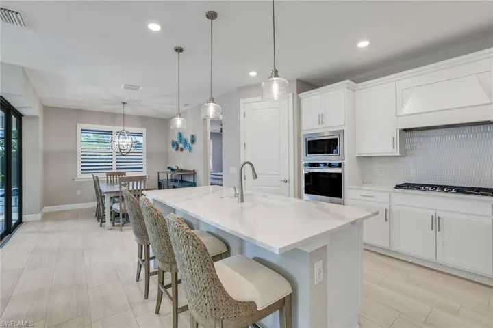 Kitchen featuring decorative backsplash, a breakfast bar, white cabinetry, stainless steel appliances, and an island with sink