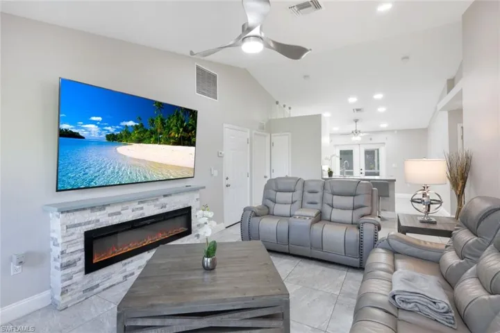 Tiled living room featuring ceiling fan, vaulted ceiling, and a stone fireplace
