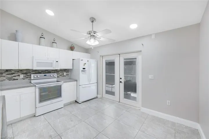 Kitchen with vaulted ceiling, white appliances, tasteful backsplash, ceiling fan, and white cabinets