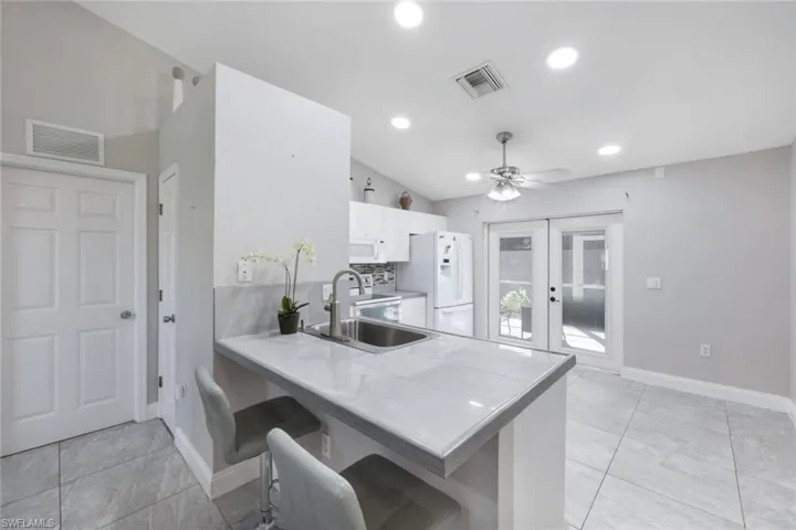 Kitchen with vaulted ceiling, white appliances, sink, kitchen peninsula, and ceiling fan