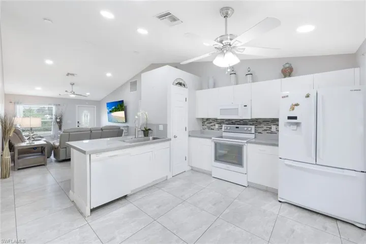 Kitchen with lofted ceiling, white appliances, kitchen peninsula, and ceiling fan