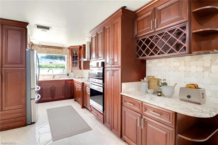 Kitchen with open shelves, tasteful backsplash, appliances with stainless steel finishes, light stone counters, and glass insert cabinets