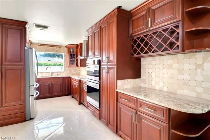 Kitchen with open shelves, backsplash, appliances with stainless steel finishes, light stone countertops, and glass insert cabinets