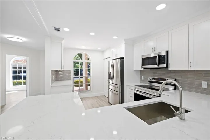 Kitchen featuring tasteful backsplash, white cabinets, a sink, stainless steel appliances, and light stone countertops