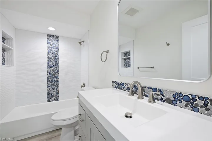 Full bathroom featuring shower / tub combination, visible vents, toilet, wood finished floors, and vanity
