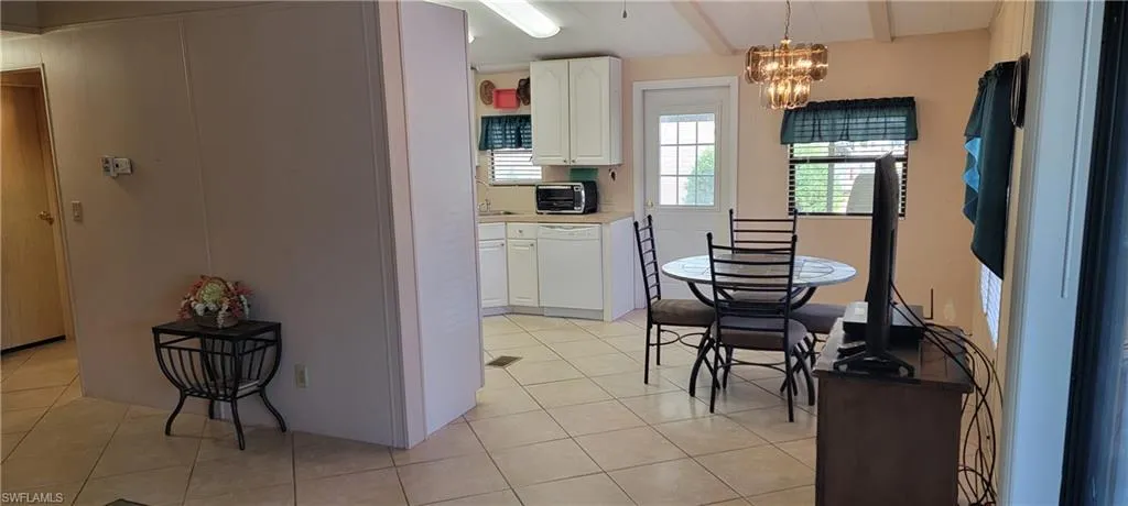 Kitchen with white dishwasher, white cabinetry, a chandelier, and light tile flooring