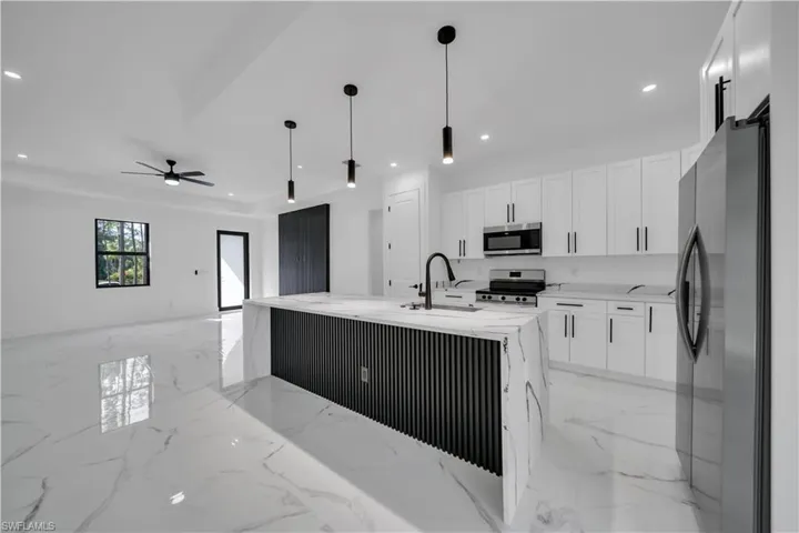 Kitchen featuring light marble finish floors, appliances with stainless steel finishes, white cabinetry, light stone counters, and a barn door