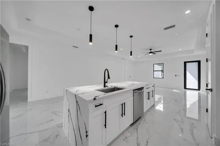 Kitchen featuring white cabinetry, a tray ceiling, hanging light fixtures, light stone countertops, and recessed lighting