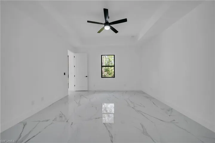 Spare room featuring a tray ceiling, light marble finish flooring, and ceiling fan