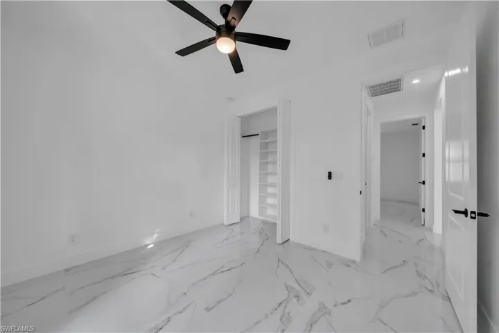 Unfurnished bedroom featuring a ceiling fan, light marble finish flooring, and a closet