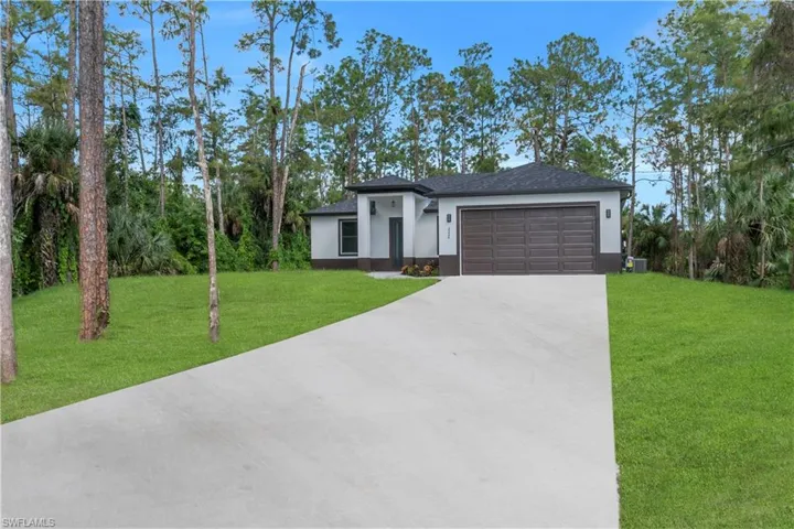View of front facade featuring a front lawn, stucco siding, concrete driveway, an attached garage, and roof with shingles