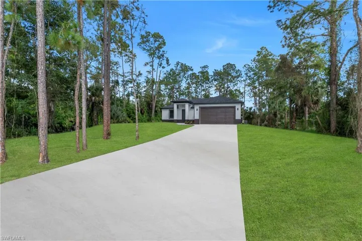 View of front of home featuring a front yard, driveway, a garage, and view of wooded area