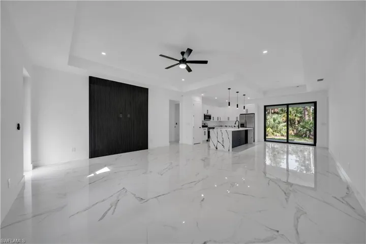 Unfurnished living room featuring a tray ceiling, recessed lighting, light marble finish flooring, and a ceiling fan