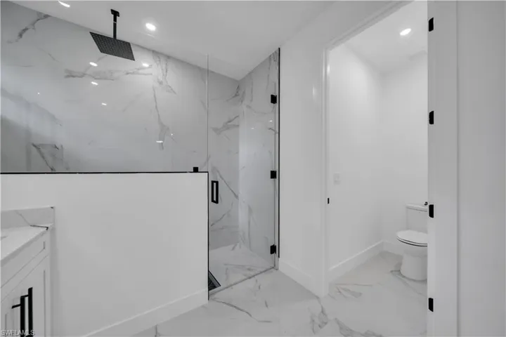 Full bathroom featuring a marble finish shower, vanity, light marble finish flooring, and recessed lighting