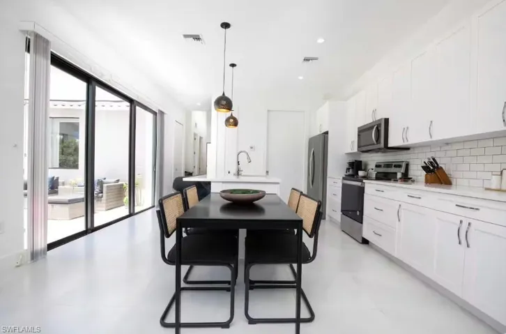 Open-concept kitchen and dining area featuring white cabinetry, subway tile backsplash, and stainless steel appliances