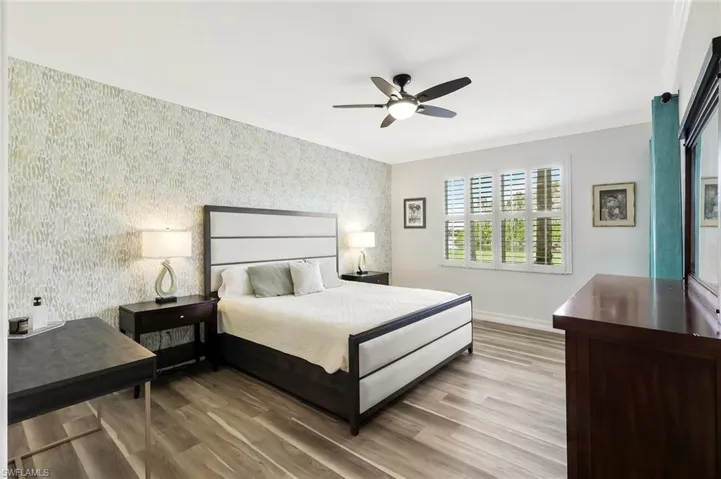 Bedroom with wallpapered walls, crown molding, wood finished floors, a ceiling fan, and an accent wall