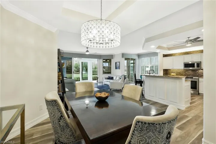 Dining area with ceiling fan, a tray ceiling, crown molding, light wood finished floors, and suspended lighting
