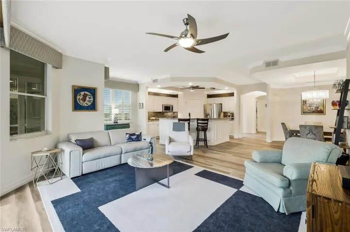 Living room featuring arched walkways, light wood-style floors, a ceiling fan, and ornamental molding