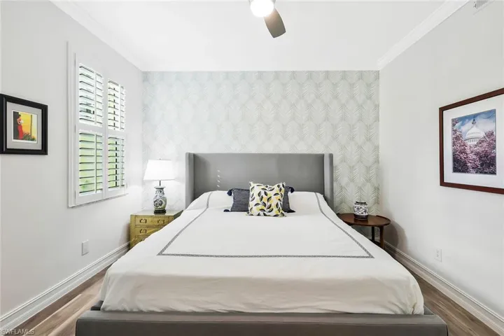 Bedroom featuring an accent wall, wood finished floors, crown molding, a ceiling fan, and wallpapered walls