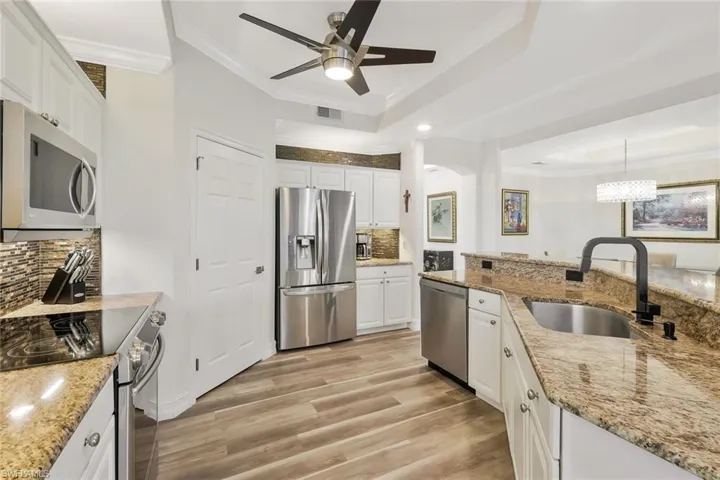 Kitchen with backsplash, stainless steel appliances, white cabinets, crown molding, and light stone countertops