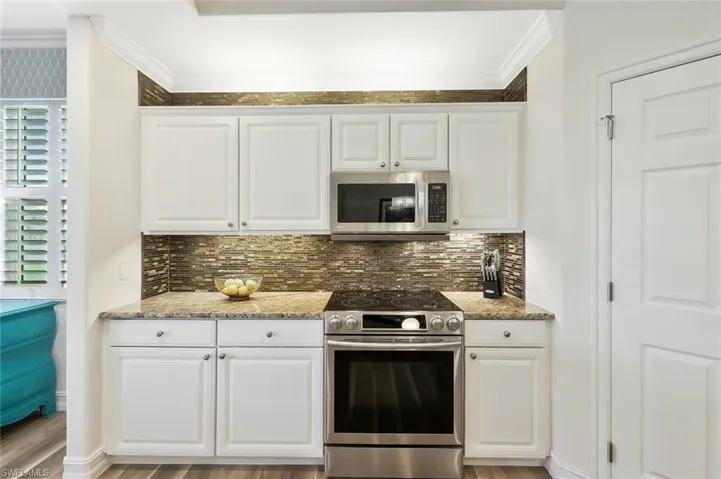 Kitchen featuring stainless steel appliances, white cabinets, light stone countertops, ornamental molding, and tasteful backsplash