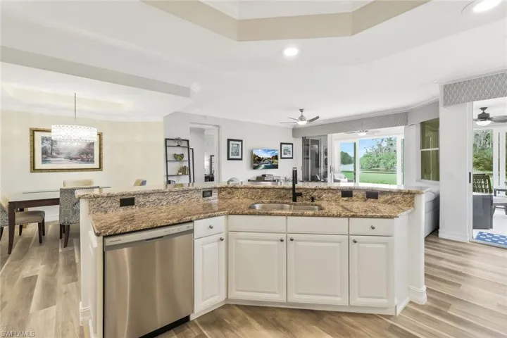 Kitchen with ornamental molding, white cabinets, stainless steel dishwasher, light wood-style flooring, and light stone countertops