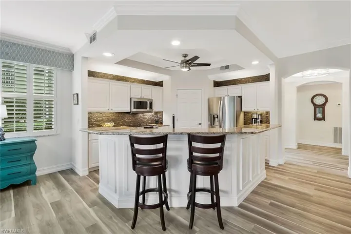 Kitchen featuring a center island with sink, white cabinetry, light stone counters, crown molding, and recessed lighting