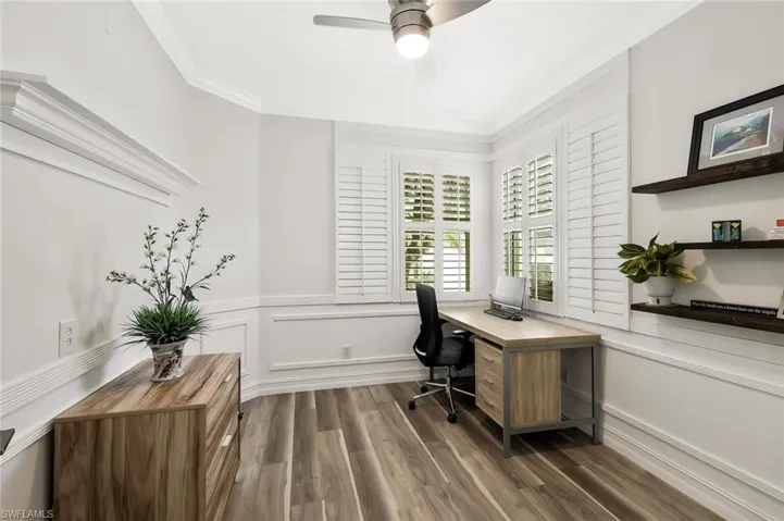 Office with dark wood-style floors, a ceiling fan, ornamental molding, a wainscoted wall, and built in study area